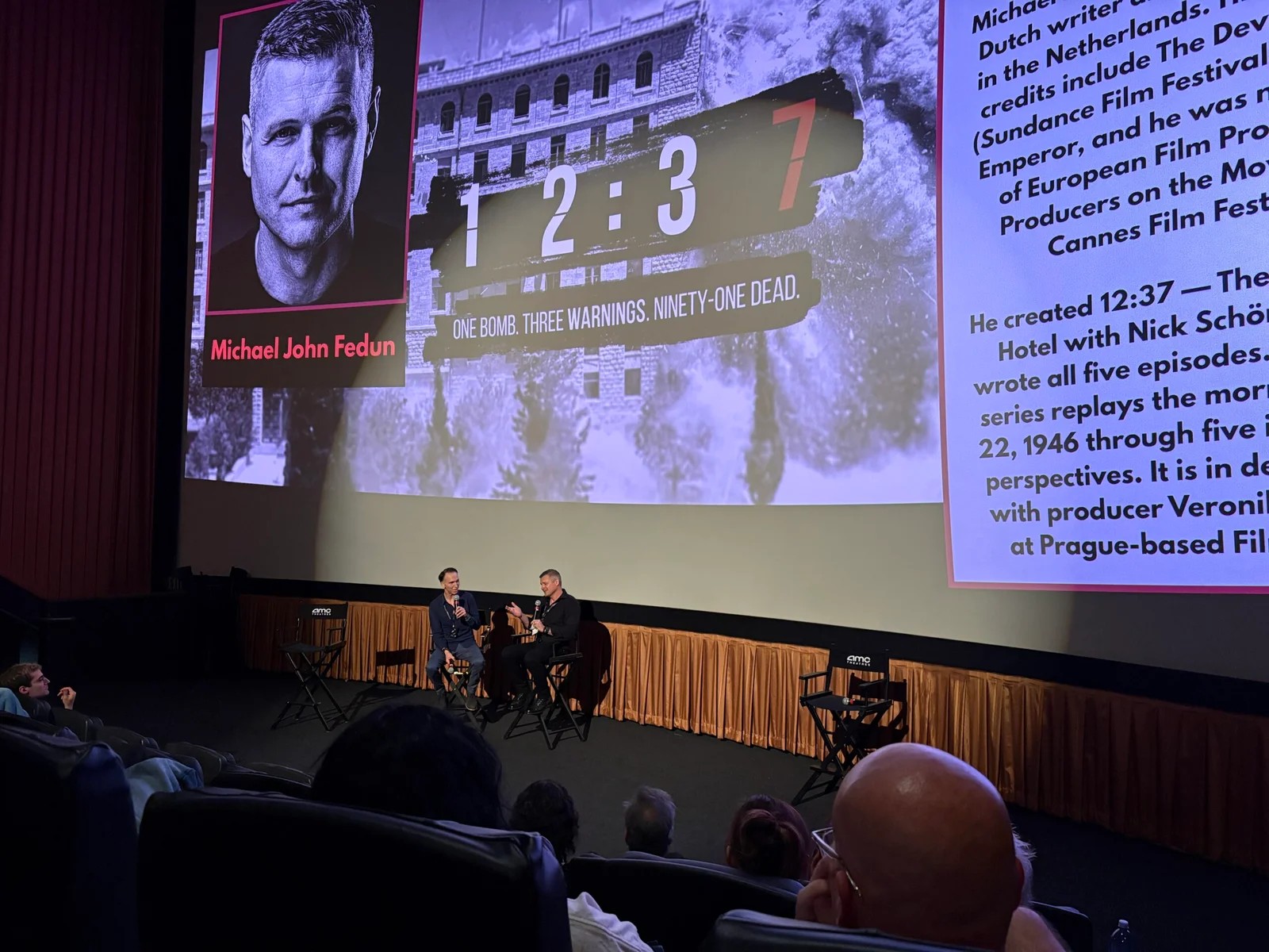 Two people seated on stage in conversation, below a screen showing the 12:37 title and a portrait captioned Michael John Fedun.